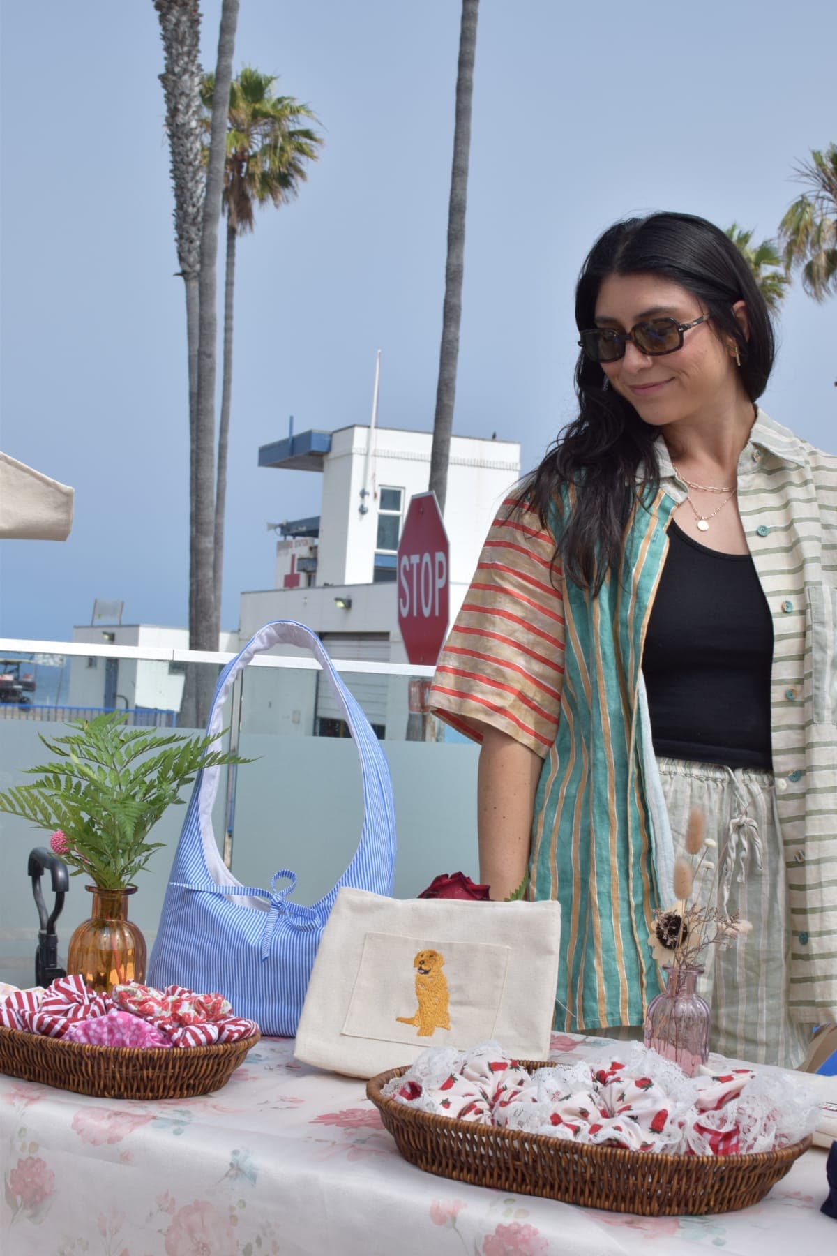 Meya at her market booth by the beach, with a cream pouch embroidered with a custom golden-retriever portrait
